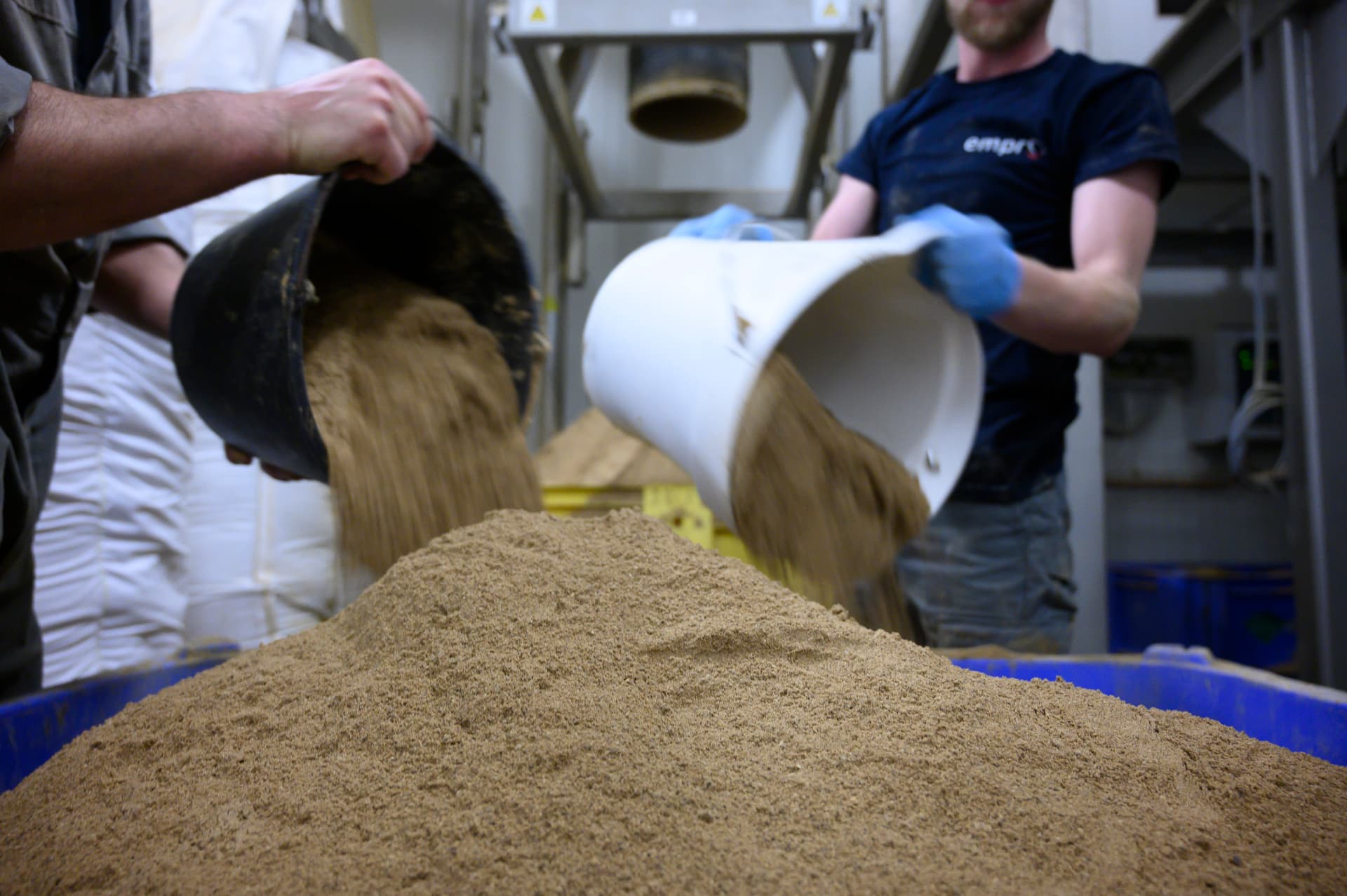 Empro operators pouring protein meal into a mixing container